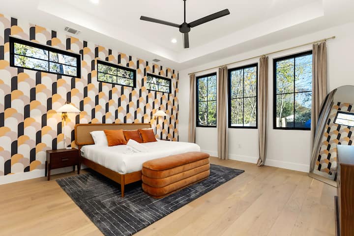 Retro-šik spálňa s manželskou posteľou!  Vstúpte do tohto žiarivého apartmánu s odvážnou vzorovanou tapetou a manželskou posteľou s oranžovou zamatovou lavicou. Vychutnajte si nadrozmerné podlahové zrkadlo, prirodzené svetlo z vysokých okien a elegantnú modernú estetiku. 