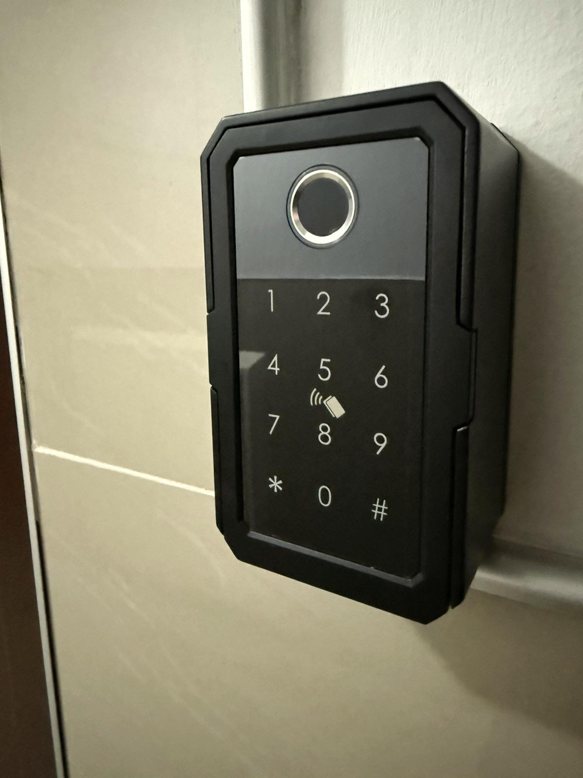 A sleek, modern keypad entry system is mounted on a wall, featuring a minimalist design with prominent numbers and a circular keyhole. The surface reflects light subtly, enhancing its contemporary appeal.