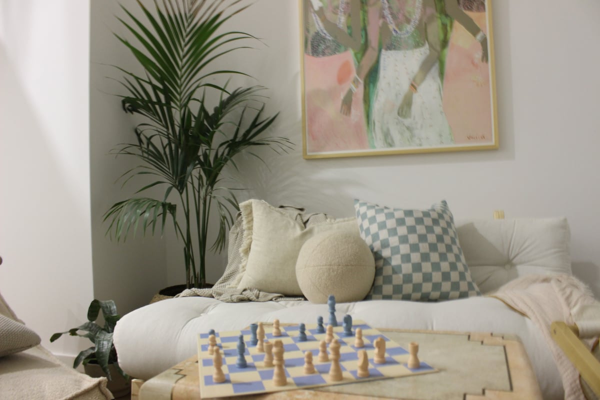 A comfortable seating area is highlighted by a large piece of artwork above a soft sofa adorned with decorative cushions. A chessboard sits on a wooden table in the foreground, while a tall plant adds a touch of greenery to the space.