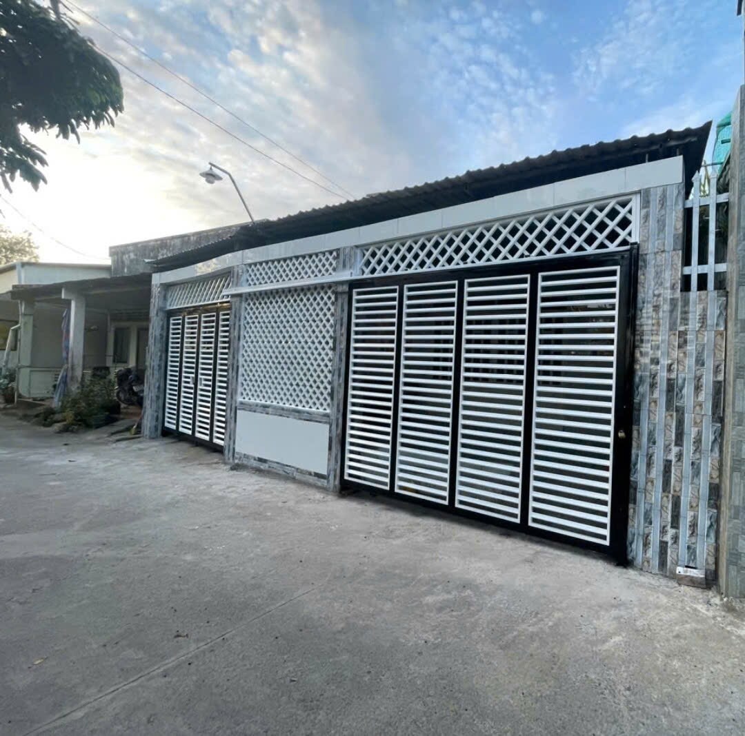 A modern enclosure is presented with horizontal white slats creating an open yet secure appearance. The exterior is composed of neutral-colored materials, complemented by a shaded roof. The setting is quiet with minimal vehicles visible along the surrounding pathway.
