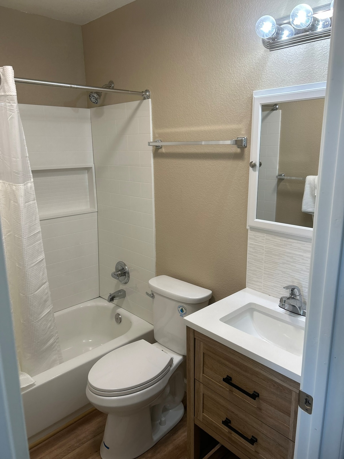 The bathroom includes a bathtub and shower combination, enhancing flexibility for bathing options. A clean toilet is positioned next to a vanity with a sink and cabinetry for storage. The space is illuminated by a light fixture above the mirror, providing adequate brightness.