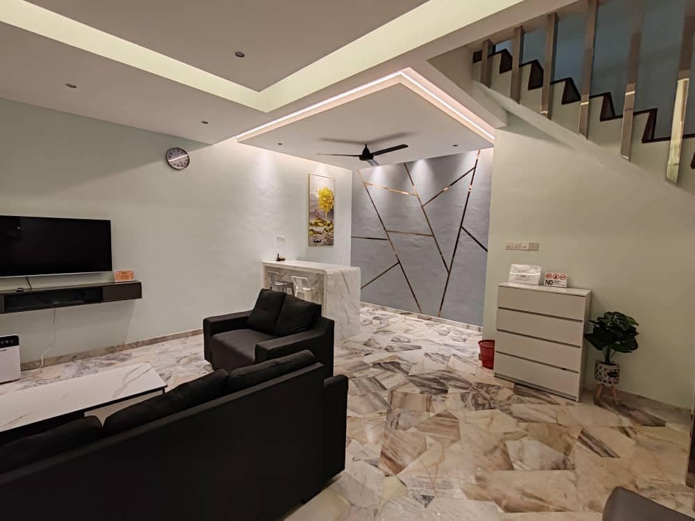 A modern living area is presented with neutral-colored walls and stylish marble flooring. A flat-screen TV is mounted on the wall opposite a set of black sofas. A dining table is positioned in front of a decorative feature wall with geometric designs, and stairs lead to the upper level.