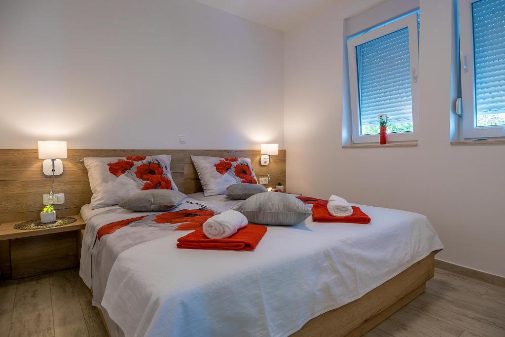 A well-appointed bedroom features a spacious bed adorned with floral-patterned bedding in red and grey. Two small windows allow natural light to fill the room. Nightstands with lamps are positioned on each side of the bed, along with neatly arranged towels.