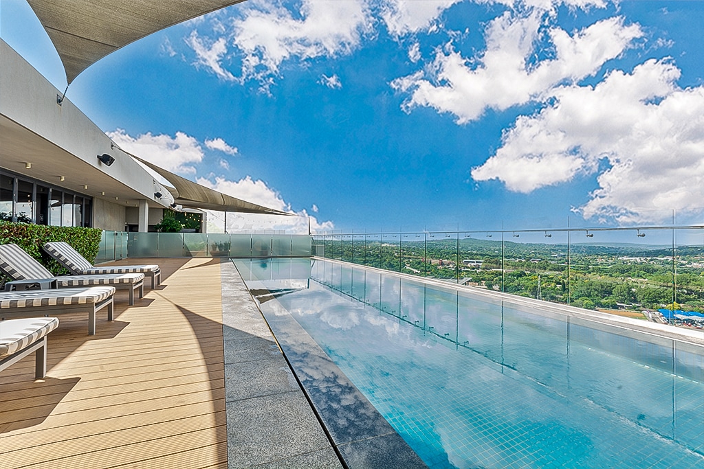 An infinity pool overlooks expansive views of the landscape, with clear skies reflected in the water. Sun loungers are positioned along the pool's edge, creating a relaxing space. The terrace is adorned with modern design elements, providing a serene outdoor area.