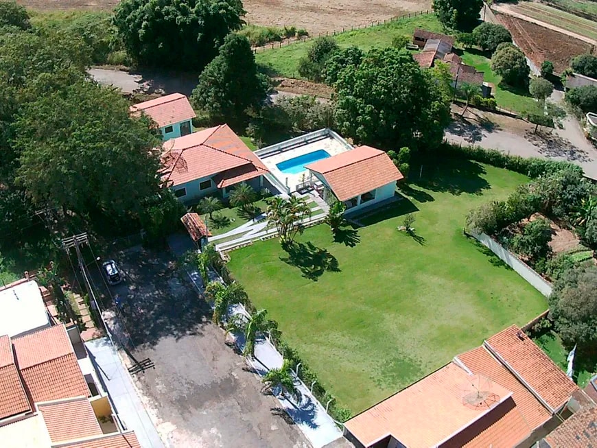 An aerial view showcases a spacious property featuring two houses, a swimming pool, and a well-maintained grassy area. Surrounding trees and paths provide a natural setting, while the nearby road is visible, indicating accessibility.