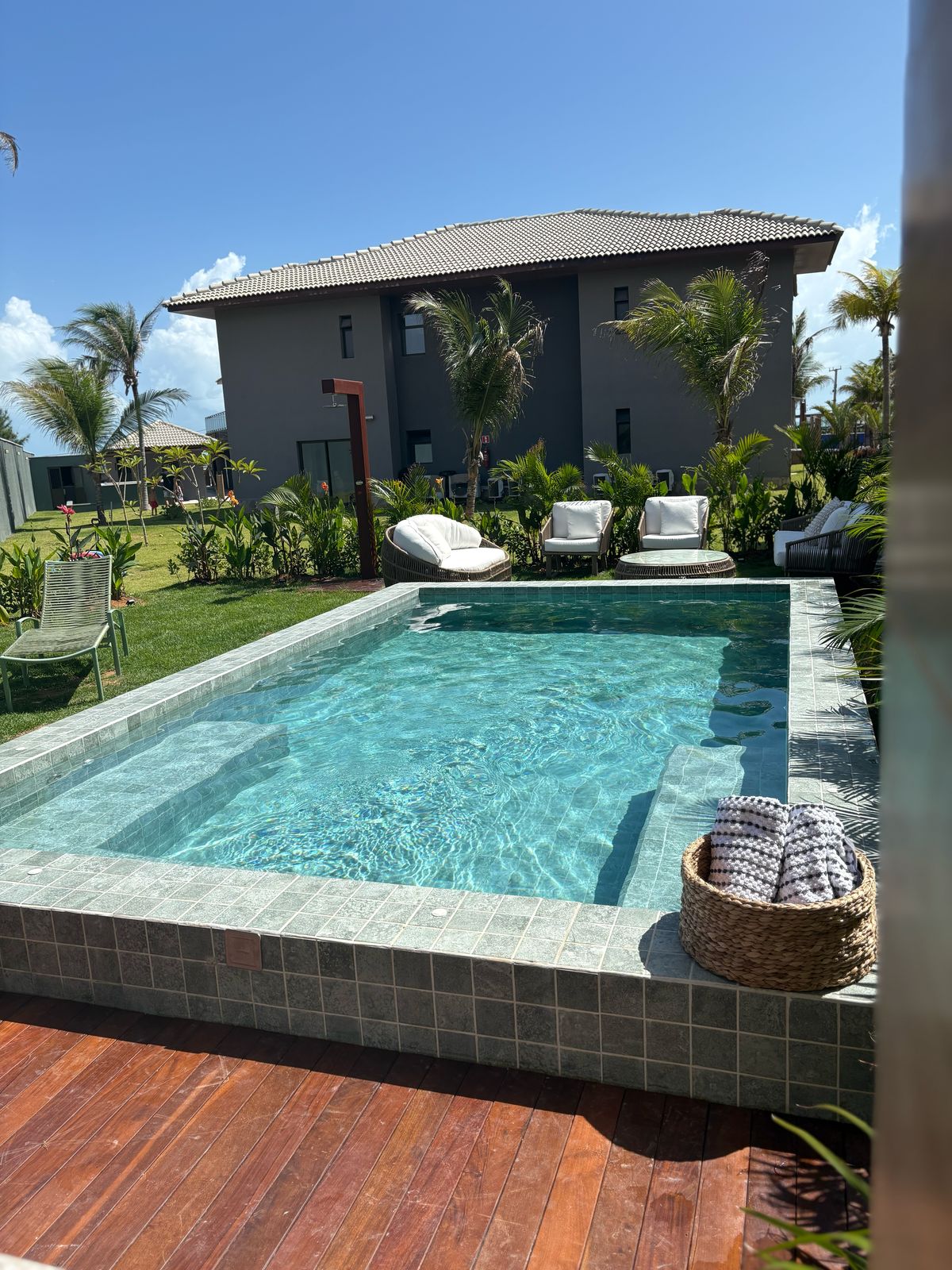 A private pool is surrounded by tropical greenery, featuring a clear blue water surface. Comfortable lounge chairs are positioned alongside the pool, inviting relaxation. The adjacent house is visible in the background, contributing to the serene outdoor setting.