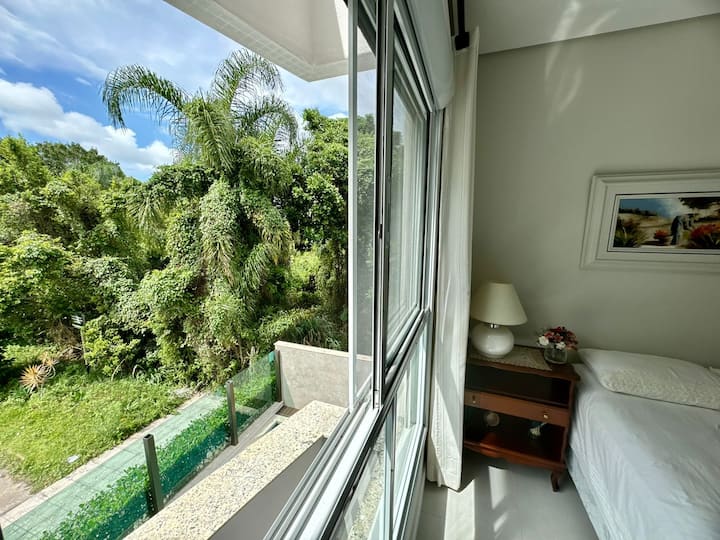 Suite con ventana grande, ubicación espaciosa, vista a la piscina y área de bosque virgen al aire libre.