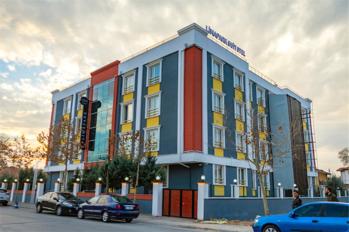 The three-story building features a modern design with a blend of blue, red, and yellow panels. Large windows allow natural light to fill the spaces. The well-maintained exterior is surrounded by trees and offers ample parking along the street.