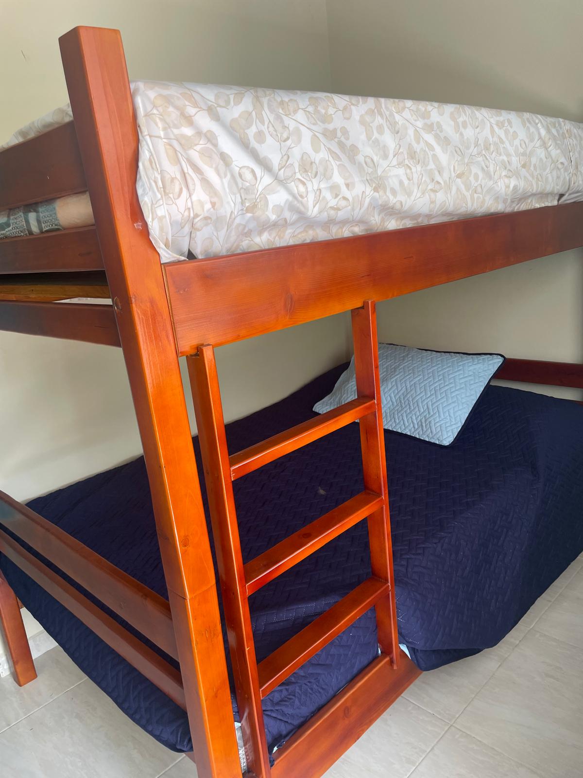 A wooden bunk bed is featured in the room, with a patterned mattress on the upper level. The lower level displays a spacious bed covered in dark blue bedding. A light-colored pillow rests against the wall, providing comfort and support.