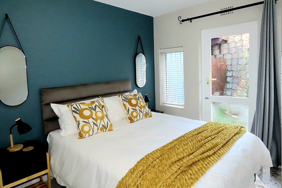 Gezellige slaapkamer met een levendige accentmuur, comfortabel bed, stijlvolle inrichting en directe toegang tot de buitenruimte. Perfect om te ontspannen na een dagje uit, met verduisteringsgordijnen en warme verlichting voor extra comfort.