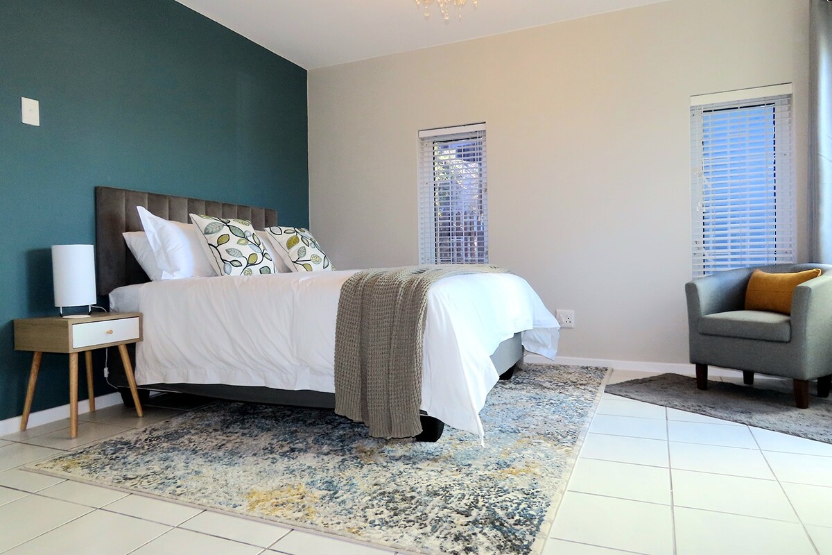 Ruime slaapkamer met een pluche bed, stijlvolle inrichting en veel daglicht. Geniet van een gezellige fauteuil, nachtlampjes en verduisterende jaloezieën voor een rustgevend verblijf.