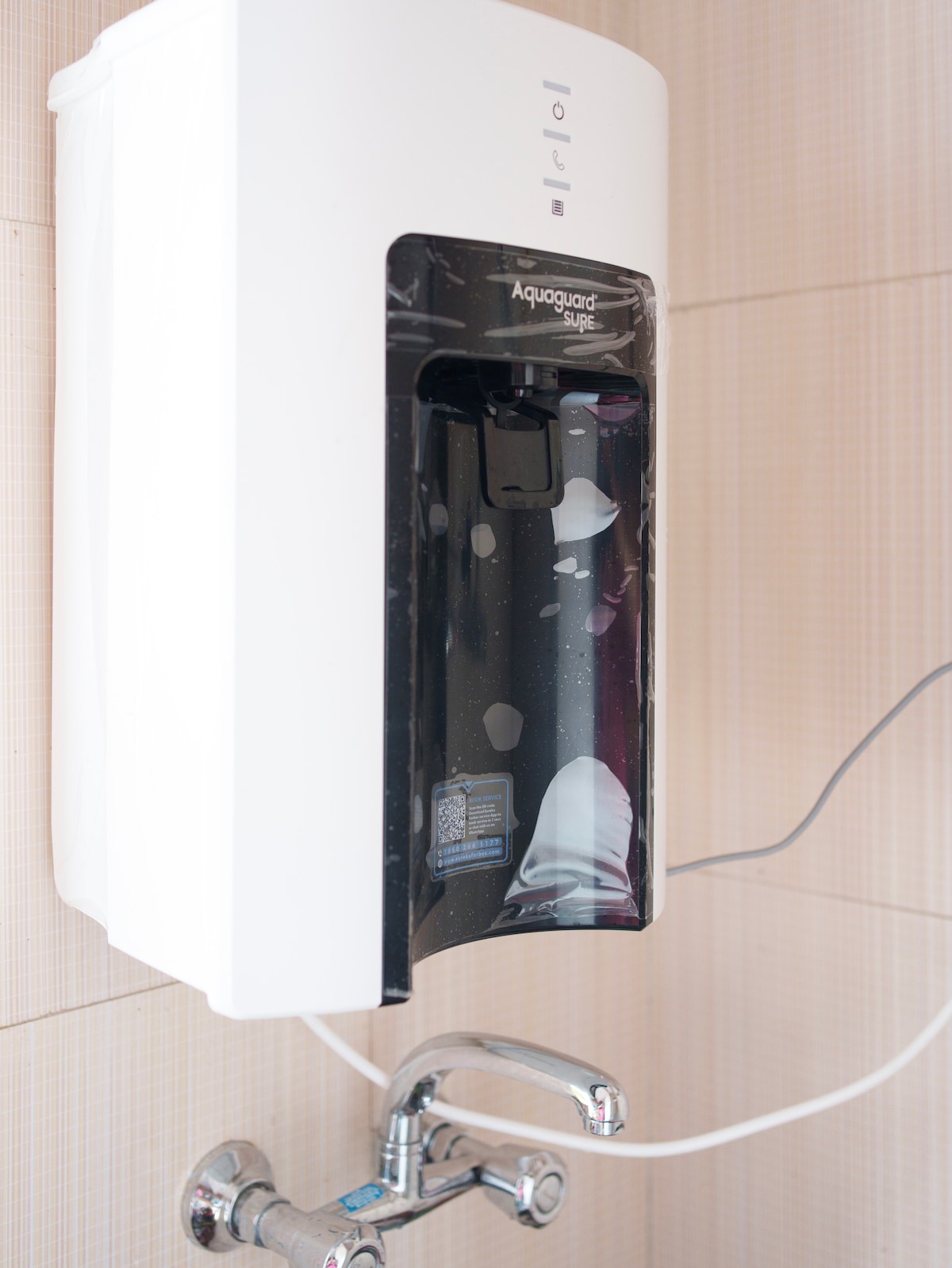 A water purification system is mounted on the wall, providing filtered drinking water. The unit features a sleek, modern design with a transparent front and a simple control panel. A faucet is visible below, ensuring easy access to clean water.