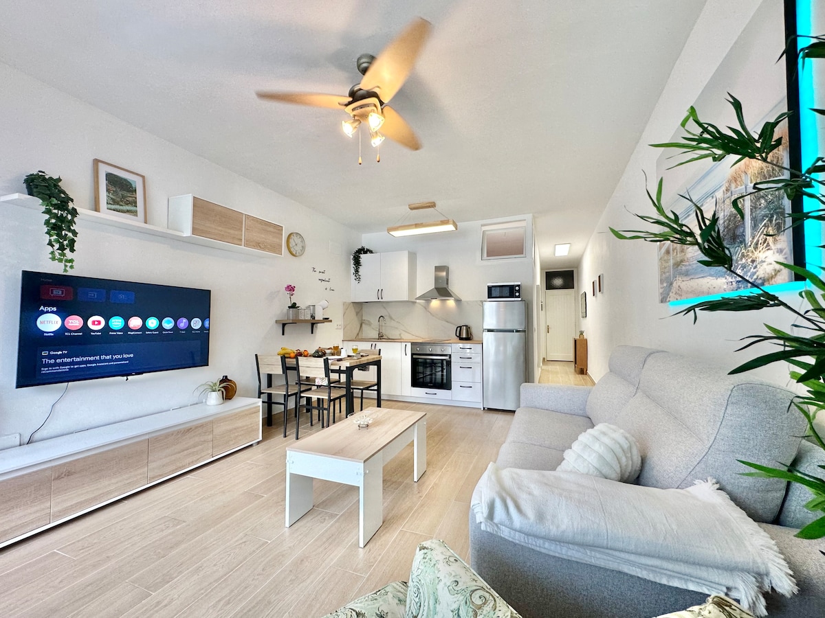 Una elegante sala de estar con un acogedor sofá, una elegante televisión para el entretenimiento y un balcón que ofrece impresionantes vistas, perfecto para la relajación y la comodidad.