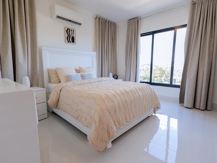 The master bedroom offers ample space to rest, with a large and comfortable bed, and plenty of natural light coming in through the window. It is a quiet retreat designed for your comfort and relaxation.
