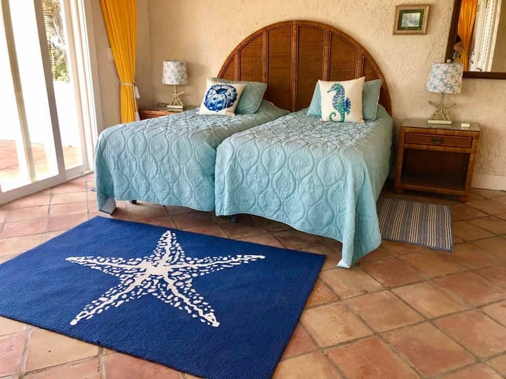 Dormitorio en la planta superior con dos camas individuales, escritorio, baño privado, aire acondicionado y ventilador de techo, y acceso directo a la terraza trasera con vistas al océano Atlántico.