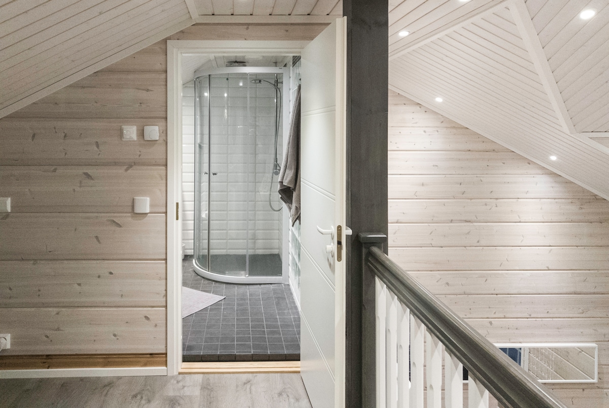 A well-lit hallway leads to a modern glass shower enclosure. Light wood walls create a natural ambiance. The stylish bathroom features tiled flooring and is complemented by soft lighting. The overall design emphasizes functionality and a clean aesthetic.