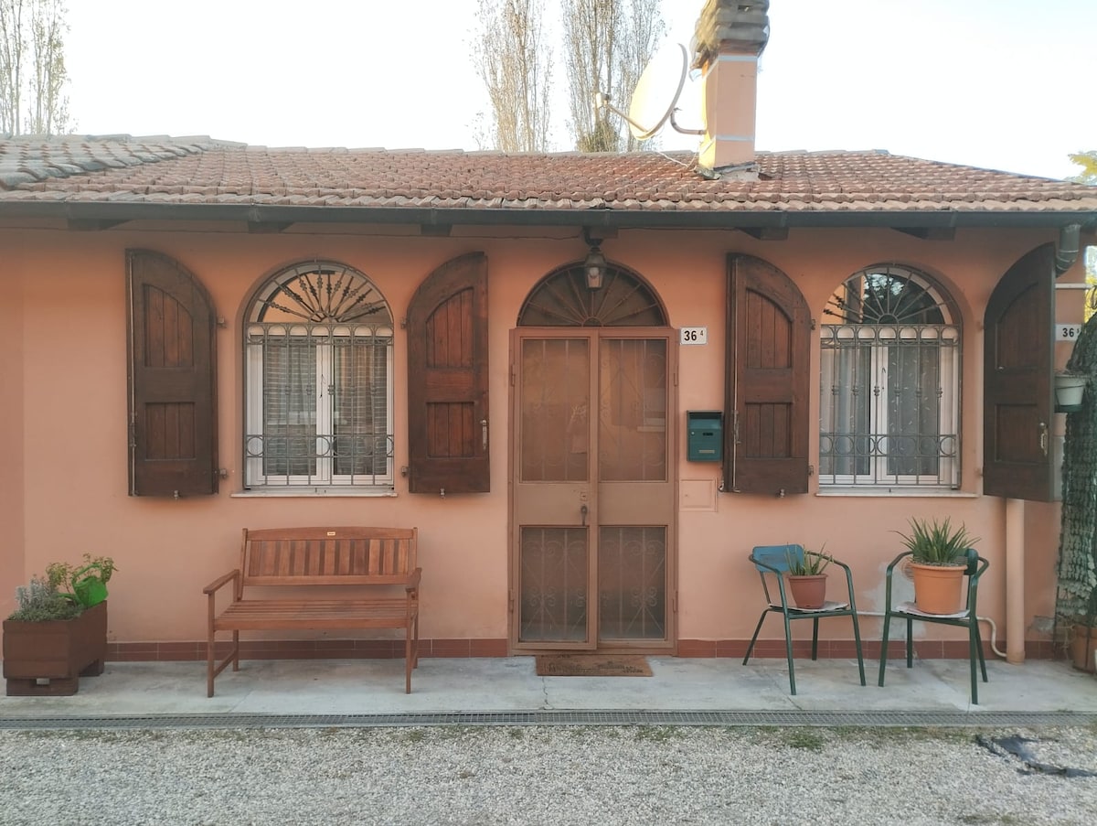 The exterior of the apartment displays a charming facade with arched windows, adorned with wooden shutters. A wooden bench sits outside, complemented by potted plants on either side, creating an inviting entrance. The gravel pathway leads directly to the main door.