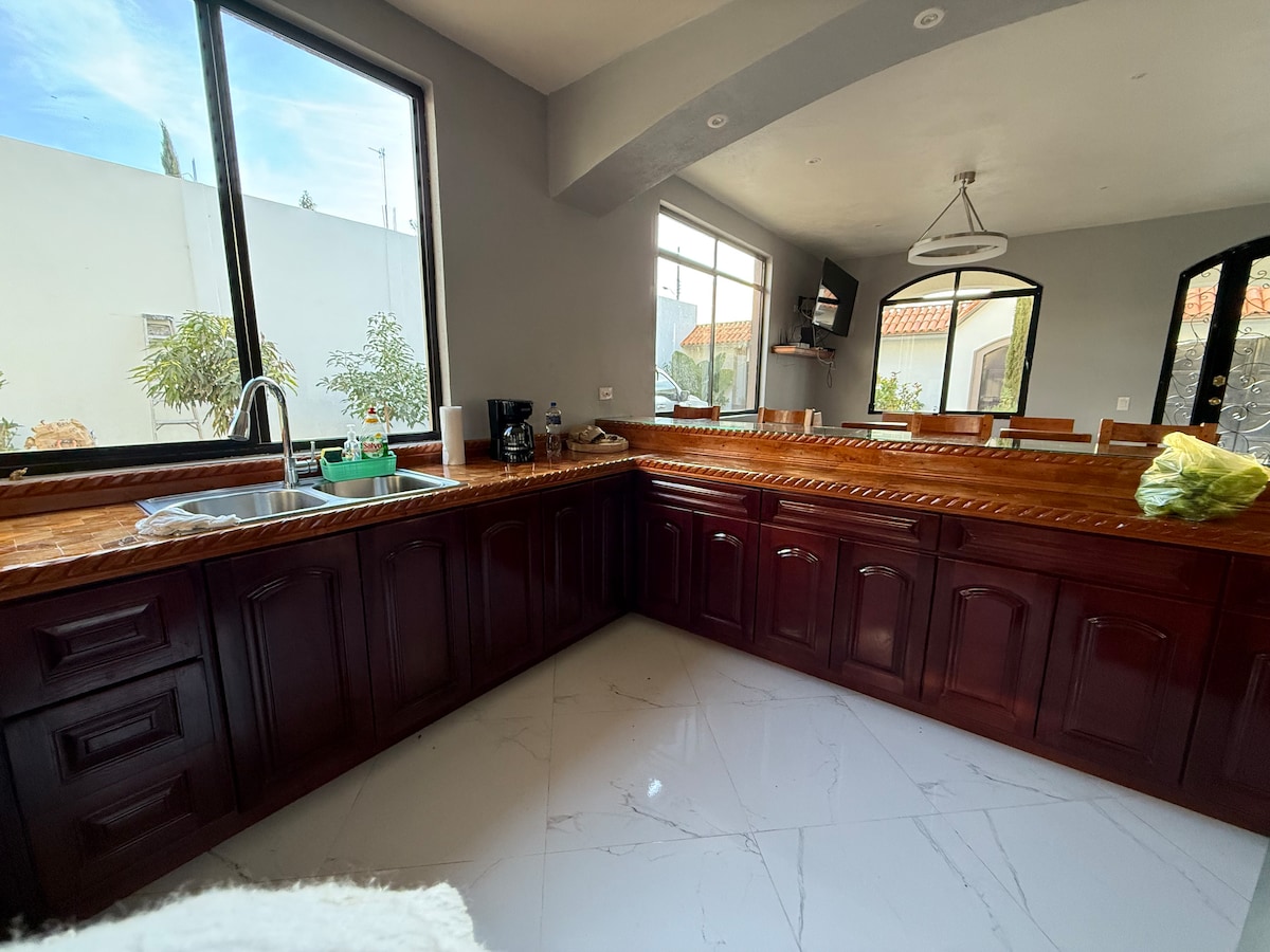 A spacious kitchen is highlighted by dark wooden cabinetry and a large countertop. Natural light fills the area through multiple windows, revealing modern appliances and a minimalistic design. The kitchen seamlessly connects to the dining area, enhancing the open layout.
