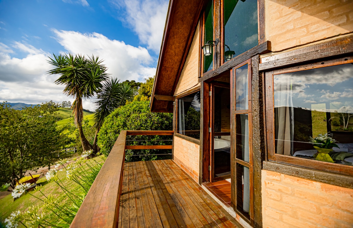 A spacious wooden balcony is featured, overlooking lush greenery and distant mountains. Large glass doors provide access to the interior, allowing natural light to fill the space. Decorative lanterns hang near the entrance, enhancing the connection between indoor and outdoor living.