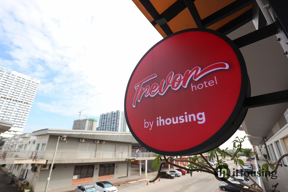 The hotel’s sign is prominently displayed, featuring the name 'Trevor Hotel' in bold lettering. The bright red circular sign contrasts with the building's exterior, which is characterized by a clean and modern design. Clear skies are visible in the background, suggesting a welcoming atmosphere.