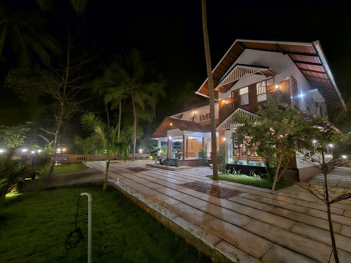 The property features a spacious outdoor area surrounded by lush greenery. The two-story structure is highlighted by a covered porch with seating. Soft lighting enhances the inviting atmosphere, creating a serene space ideal for relaxation.