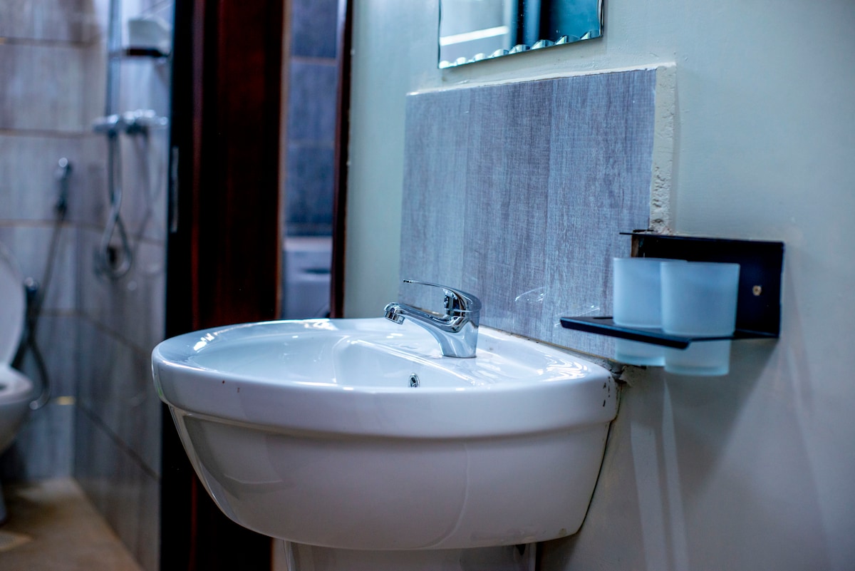 A clean bathroom space features a modern sink with a polished faucet, set against a light-colored wall. Two clear glasses are positioned on a sleek shelf nearby. The area is designed for functionality and convenience, with additional bathroom fixtures visible in the background.