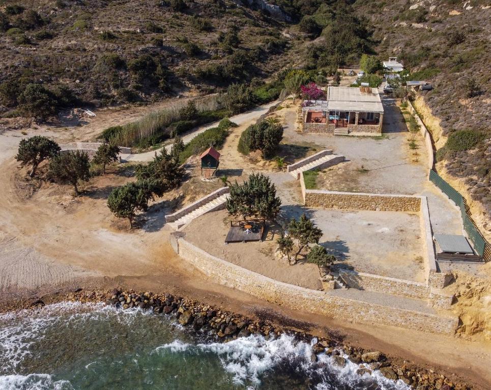 An aerial view of a coastal property reveals a spacious area featuring a house surrounded by natural vegetation and pathways. A stone wall delineates the perimeter, while the open landscape transitions to a rocky shoreline, providing a serene connection to the sea.