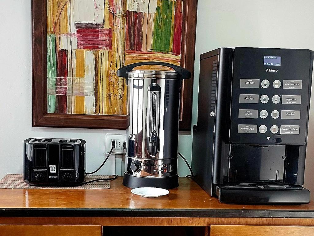 A countertop is equipped with a coffee maker and a stainless steel kettle, alongside a black toaster. A colorful abstract painting is displayed on the wall above, adding visual interest to the space.