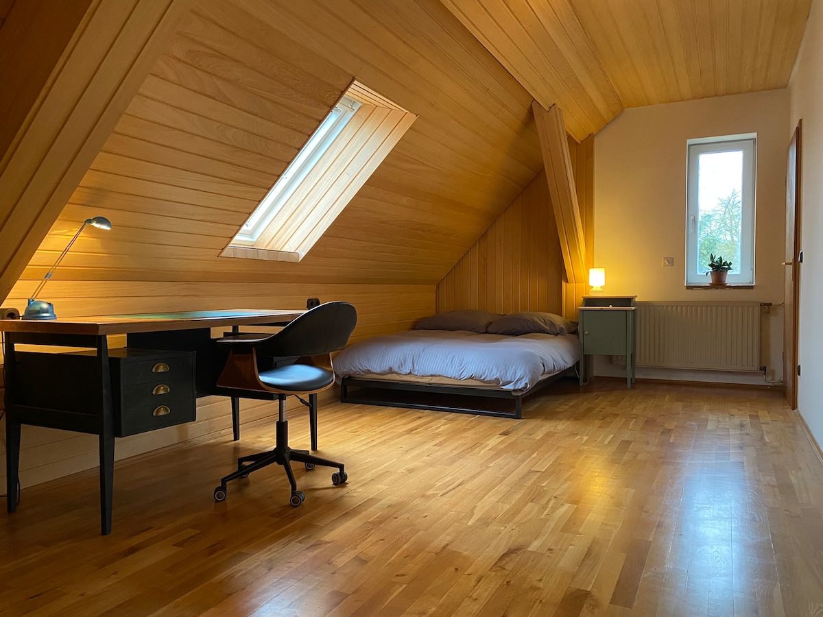 Spavaća soba s bračnim krevetom, radnim stolom i stalkom za odjeću s vješalicama.