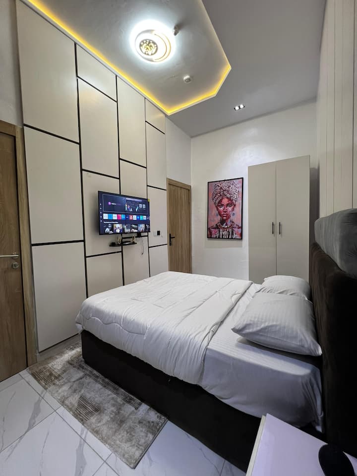Dormitorio moderno con una cama cómoda, televisor inteligente, armario elegante, luces LED en el techo y arte mural elegante... perfecto para descansar y ver vídeos en streaming.