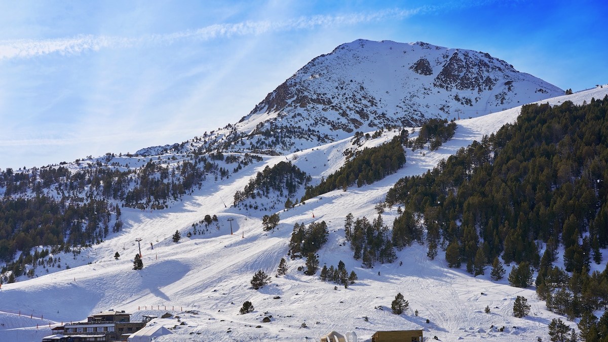 A snow-covered mountain rises against a clear blue sky, featuring slopes lined with trees. The terrain showcases a mix of gentle and steep areas, hinting at skiing opportunities. The view captures the peaceful expanse of winter scenery in the Vall d'Incles region.