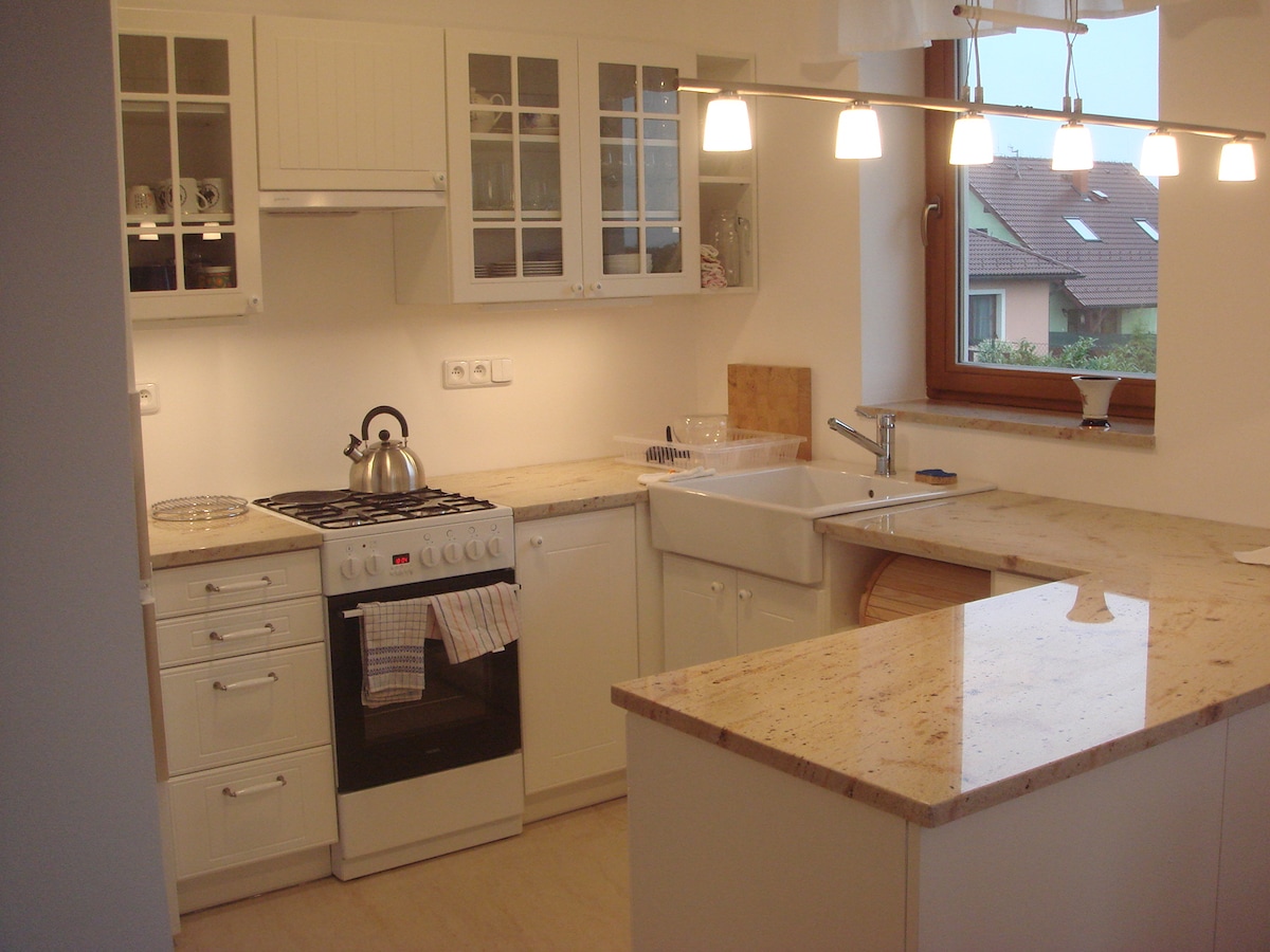 A well-appointed kitchen features white cabinetry and a spacious granite countertop. A stainless steel stove and an integrated sink are visible, along with glass-fronted cabinets displaying dishware. Soft lighting hangs above the countertop, creating an inviting atmosphere for meal preparation.
