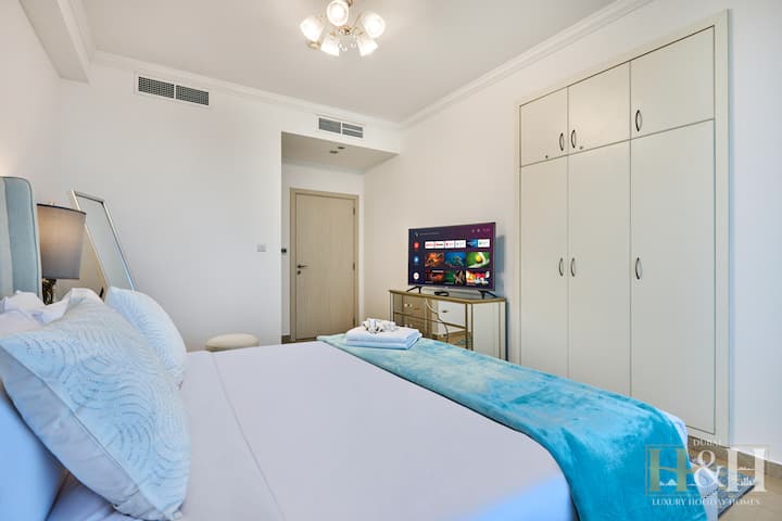 Moderno dormitorio con un elegante televisor inteligente montado en la pared, almacenamiento espejado y elegantes gabinetes blancos.