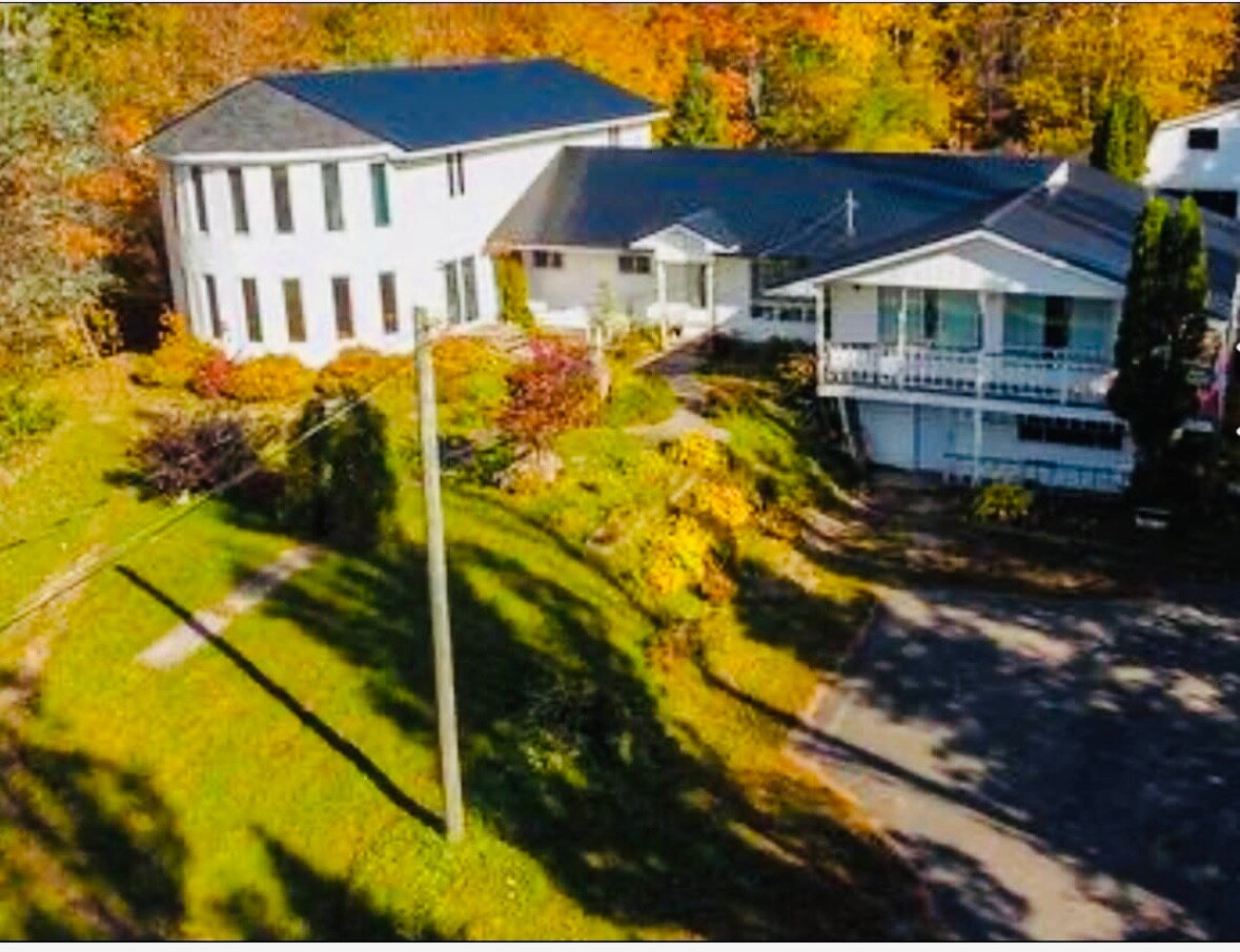 An aerial view captures a spacious property featuring a modern two-story home with large windows, surrounded by colorful autumn foliage. Lush green lawns and well-maintained landscaping complement the inviting exterior. A driveway leads toward the welcoming entrance of the residence.