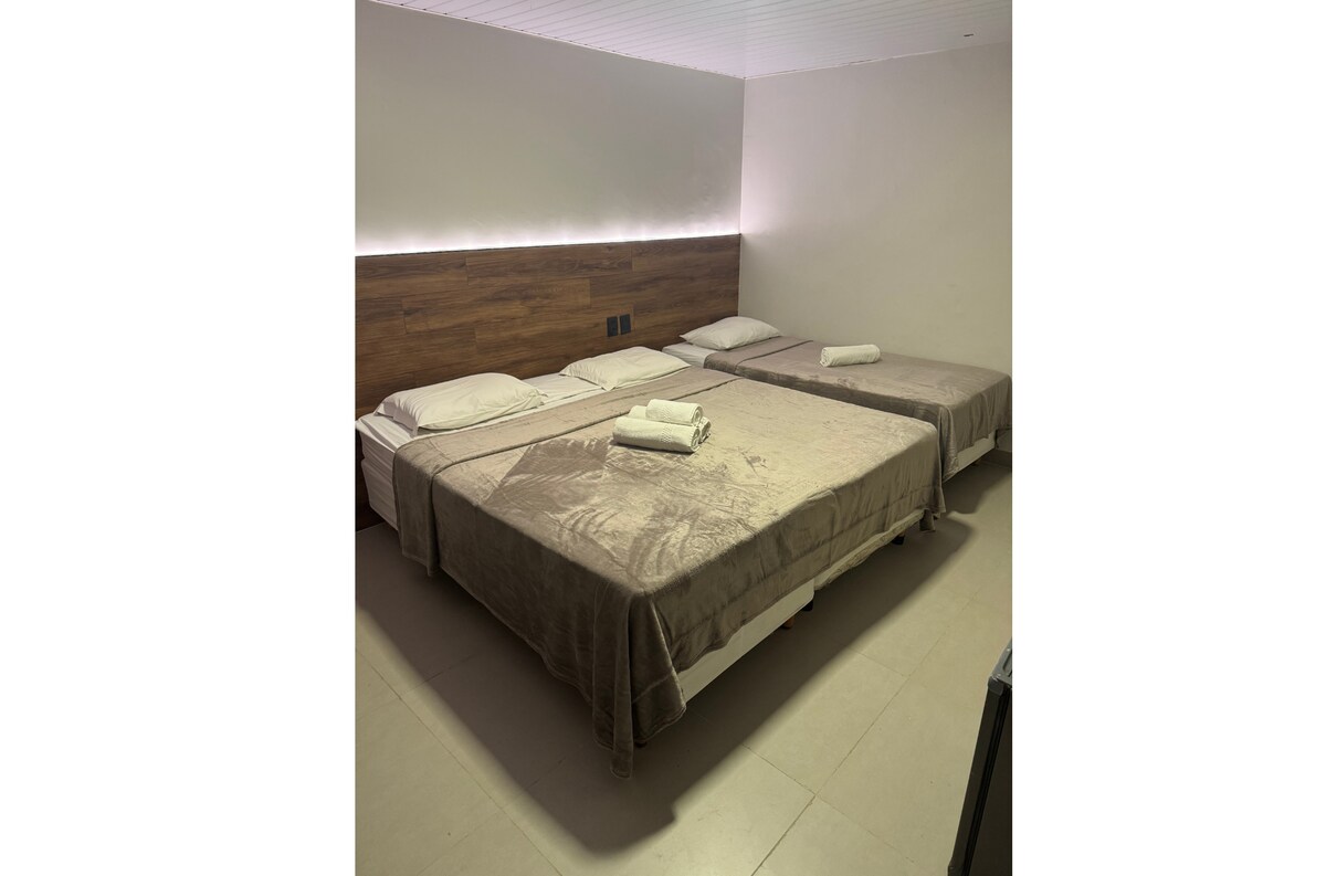 The sleeping area features two spacious beds covered with soft, neutral-toned linens and accompanied by neatly rolled towels. A subtle ambient light runs along the wall behind the beds, creating a calm and relaxed environment.