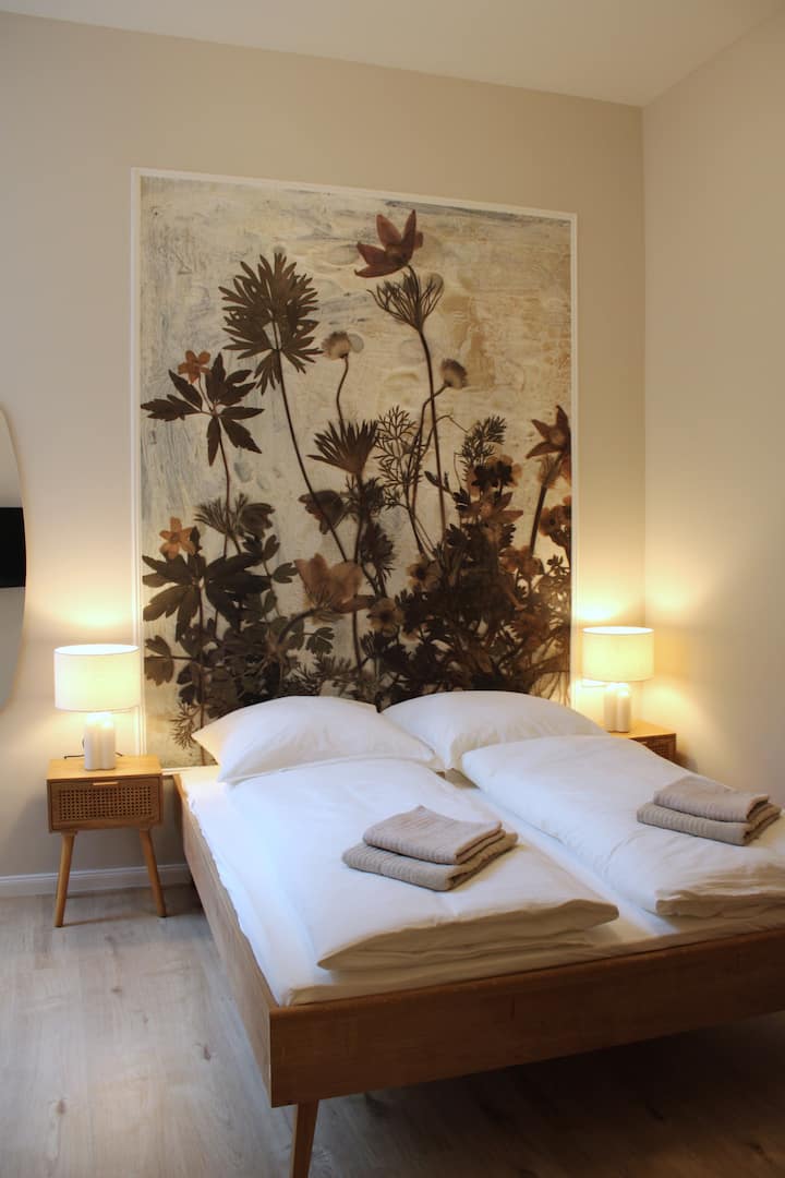 El dormitorio es un refugio tranquilo con una cómoda cama doble (160 cm de ancho) y un televisor inteligente. Los muebles sencillos y modernos crean un ambiente relajado. Ideal para noches relajantes y horas acogedoras frente a la televisión.