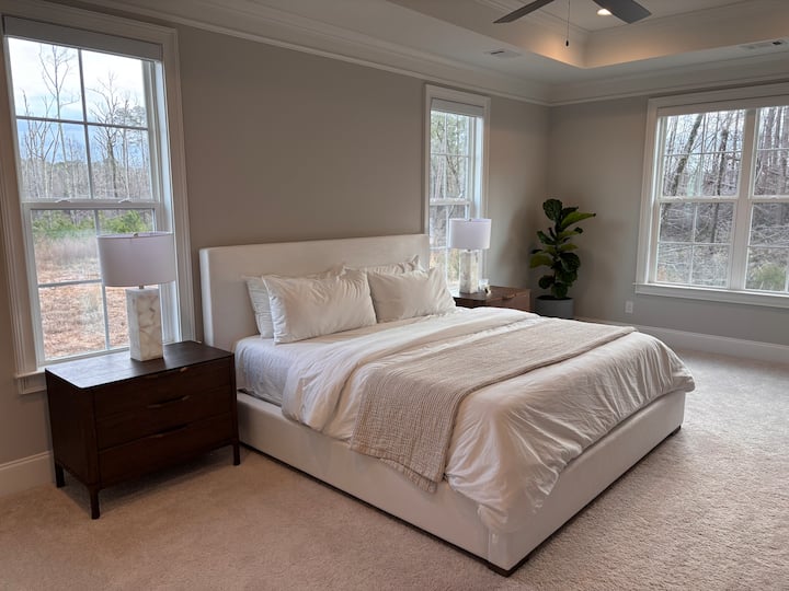 غرفة نوم رئيسية واسعة تتميز بأثاث من طراز Restoration Hardware وإطلالات هادئة على الغابات وإضاءة طبيعية خفيفة. تُكمل ستائر التعتيم الآلية وحمام داخلي على طراز السبا مع دش زجاجي وحوض استحمام عميق وخزانة ملابس خاصة هذا الملاذ الهادئ.