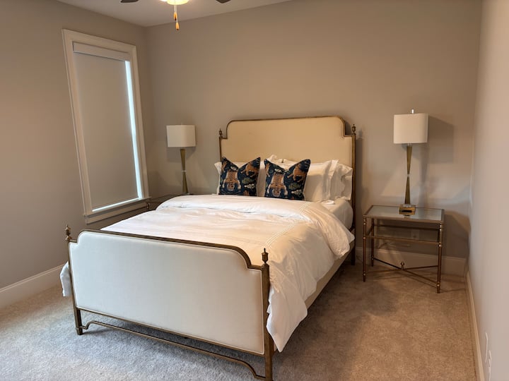 جناح ضيوف في الطابق السفلي يضم سريرًا بحجم كوين وتفاصيل نحاسية أنيقة وستائر تعتيم آلية. تحتوي على حمام داخلي خاص وخزانة ملابس، مما يوفر راحة وراحة للضيوف الزائرين.