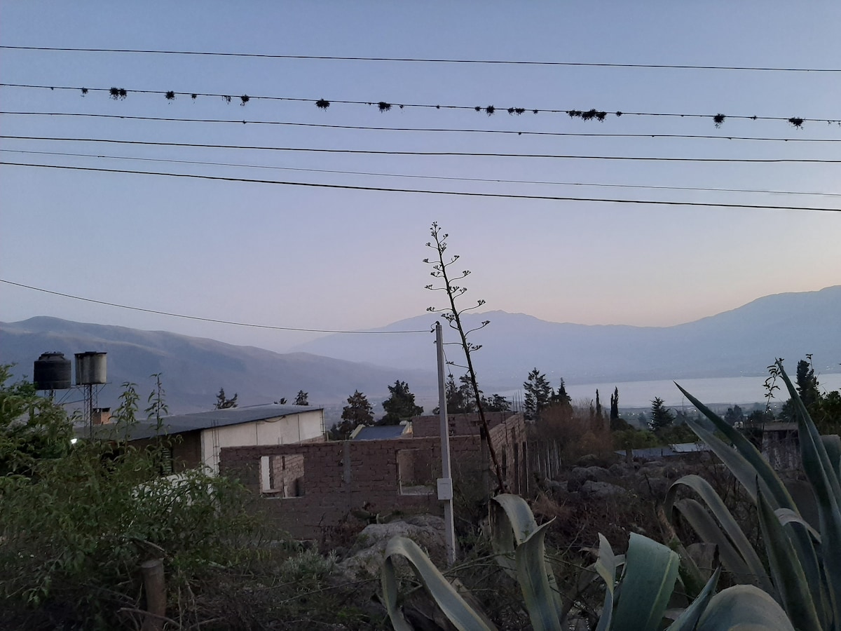 A serene landscape captures the transition from day to night, with distant mountains bathed in soft colors. Power lines are visible, adorned with silhouettes of birds, while a mix of vegetation in the foreground adds to the natural setting.