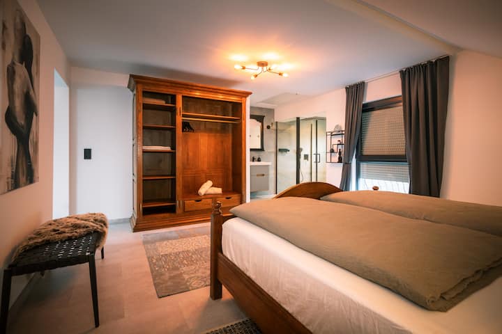 Útulná veľká spálňa s manželskou posteľou veľkosti King a elegantnou vlastnou kúpeľňou s veľkou sprchou s dažďovou sprchou.