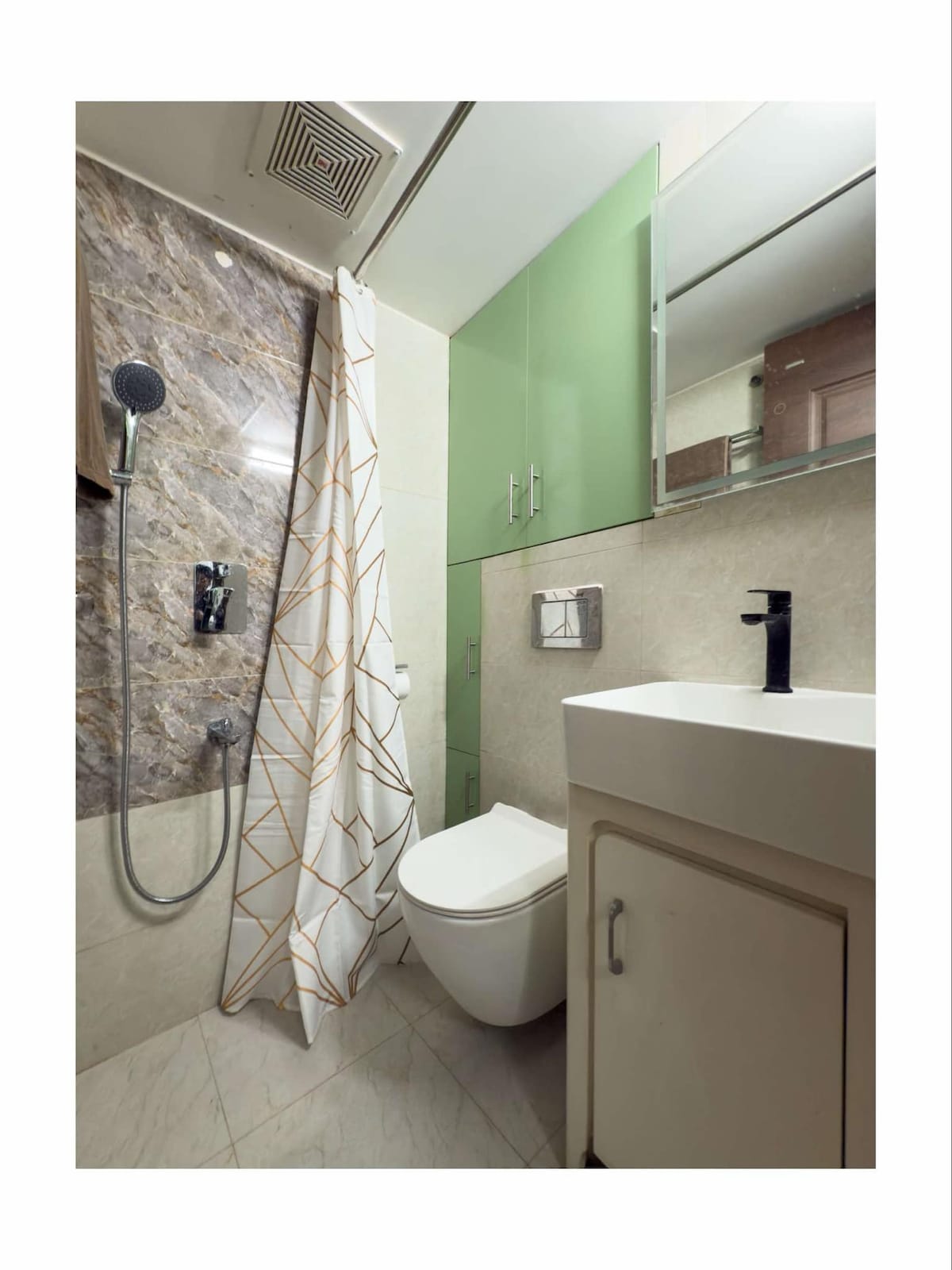 A modern bathroom is presented with a sleek design. A shower with a rainfall showerhead is featured alongside a contemporary toilet. The space includes a white sink with a dark faucet and storage cabinets. A decorative shower curtain adds a subtle pattern.