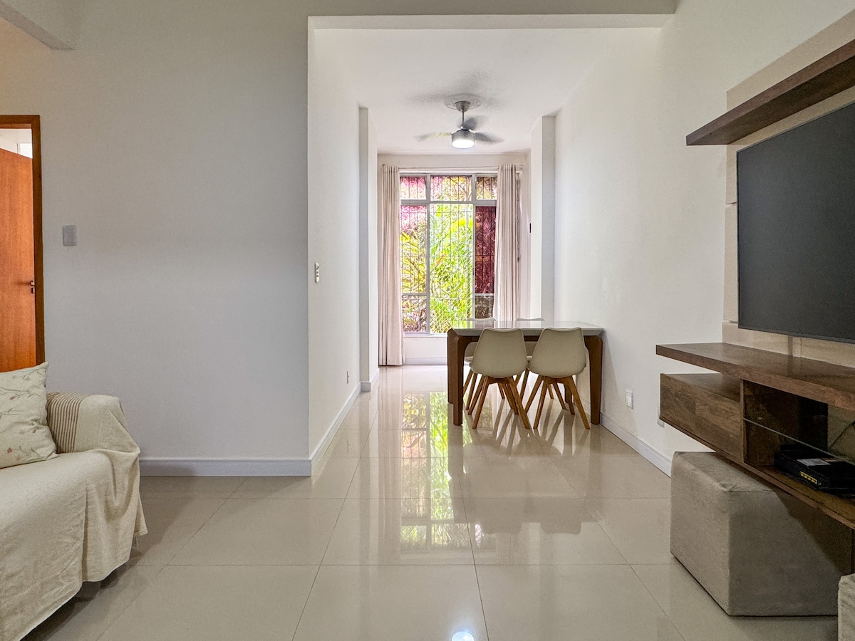 A well-lit living area features a comfortable sofa and a dining table with chairs. Large glass doors provide access to a balcony, allowing natural light to fill the space. The polished floor reflects the gentle glow from overhead lighting, creating a warm and inviting ambiance.