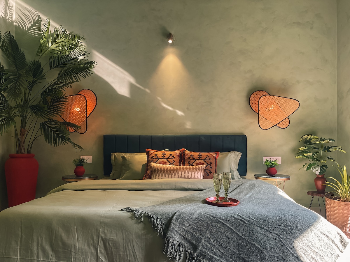 A calming bedroom features a spacious bed adorned with neutral linens and decorative pillows. Two woven lighting fixtures cast a warm glow, while potted plants add touches of greenery. Textured walls enhance the room's aesthetic, creating a serene environment.