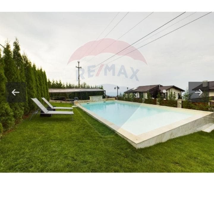 A large, heated swimming pool is set against a backdrop of manicured greenery, offering a relaxing space for leisure. Two lounge chairs are positioned on the grass nearby, providing an inviting spot for sunbathing or relaxation.