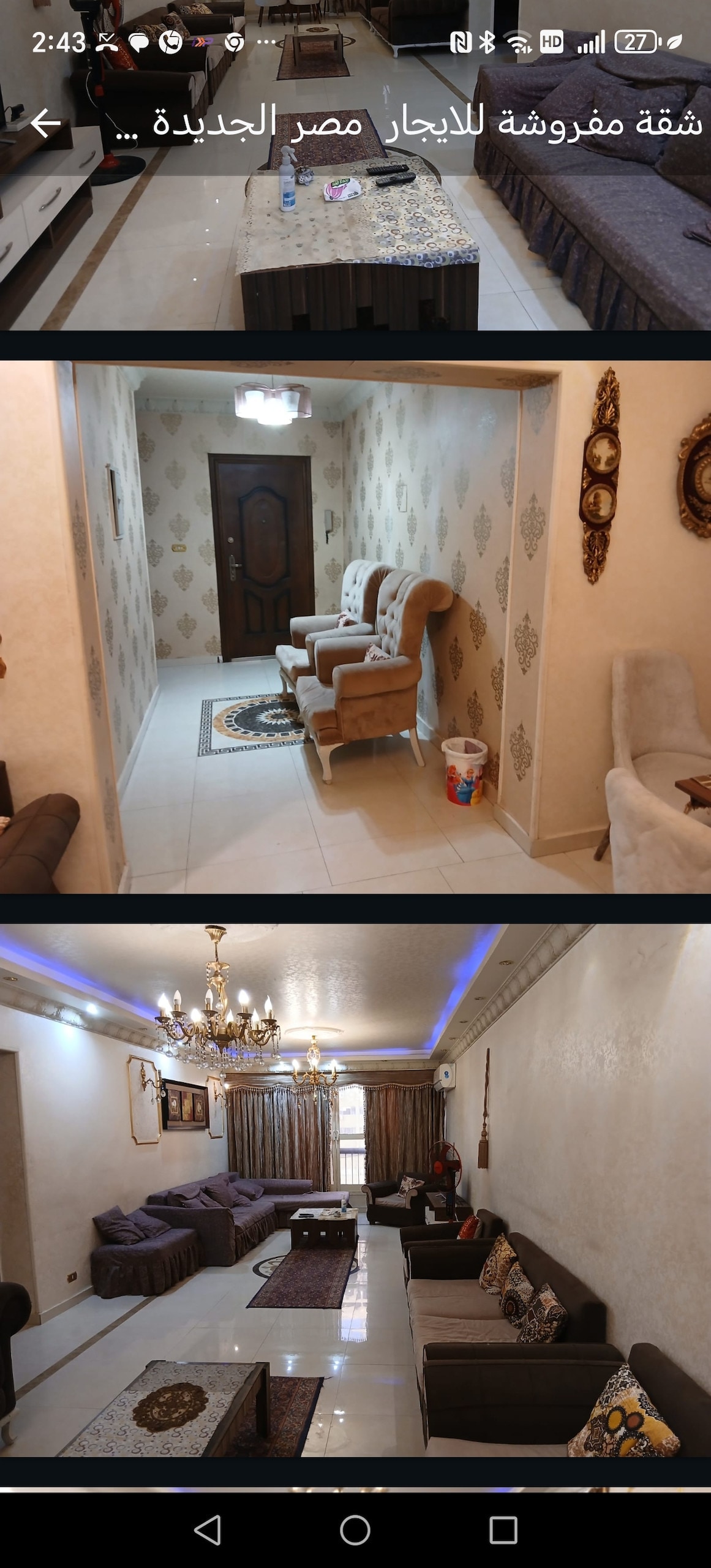A spacious living area is showcased, featuring a large sofa and multiple armchairs arranged around a coffee table. Decorative accents, including artwork and cushions, are evident. A chandelier adds elegance, while natural light filters through large windows covered with curtains.