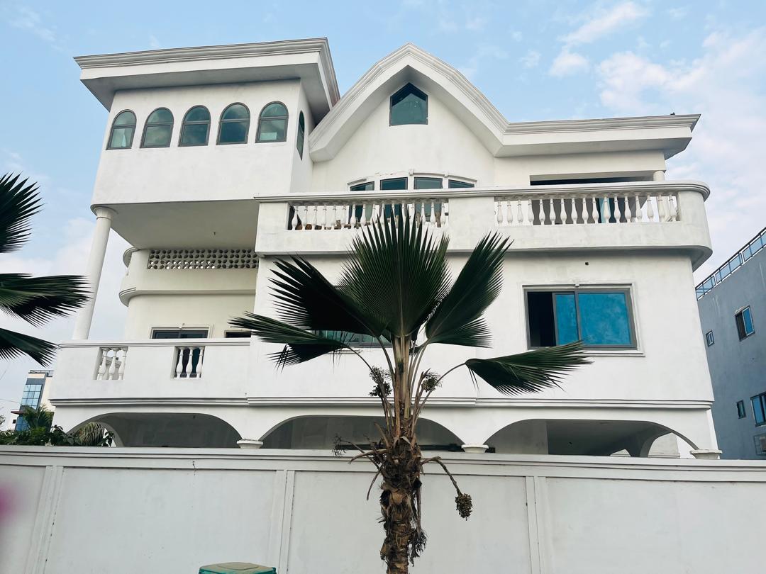 The exterior of a unique white building is highlighted, featuring multiple arched windows and balconies. Palm trees are positioned in the foreground, contrasting with the clean lines of the structure. The sky above is clear, complementing the architectural design.