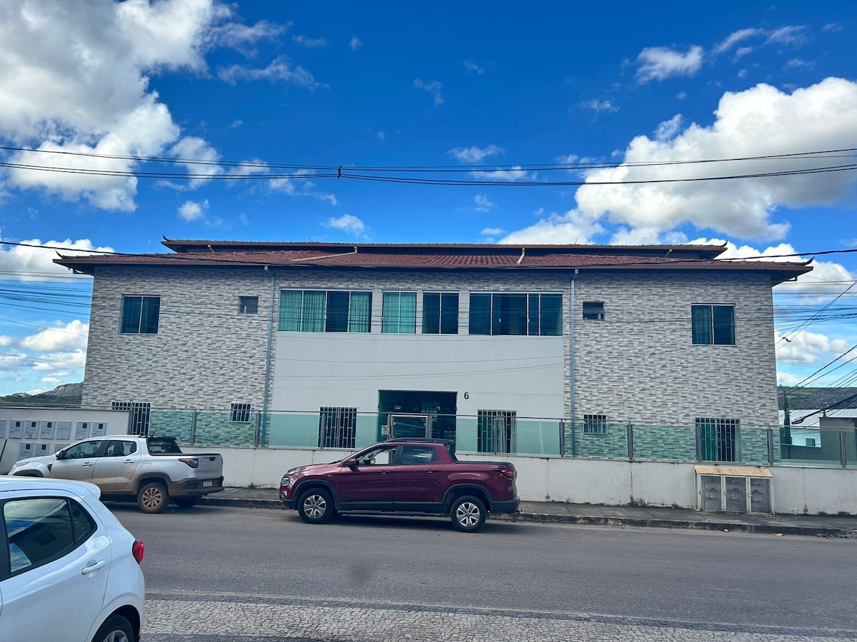 The exterior of a multi-level building is visible, featuring a modern design with large windows. The facade is clad in light-colored materials, and a harmonious blend of textures is evident. A clear blue sky is seen above, contrasting with the structure's neutral tones.