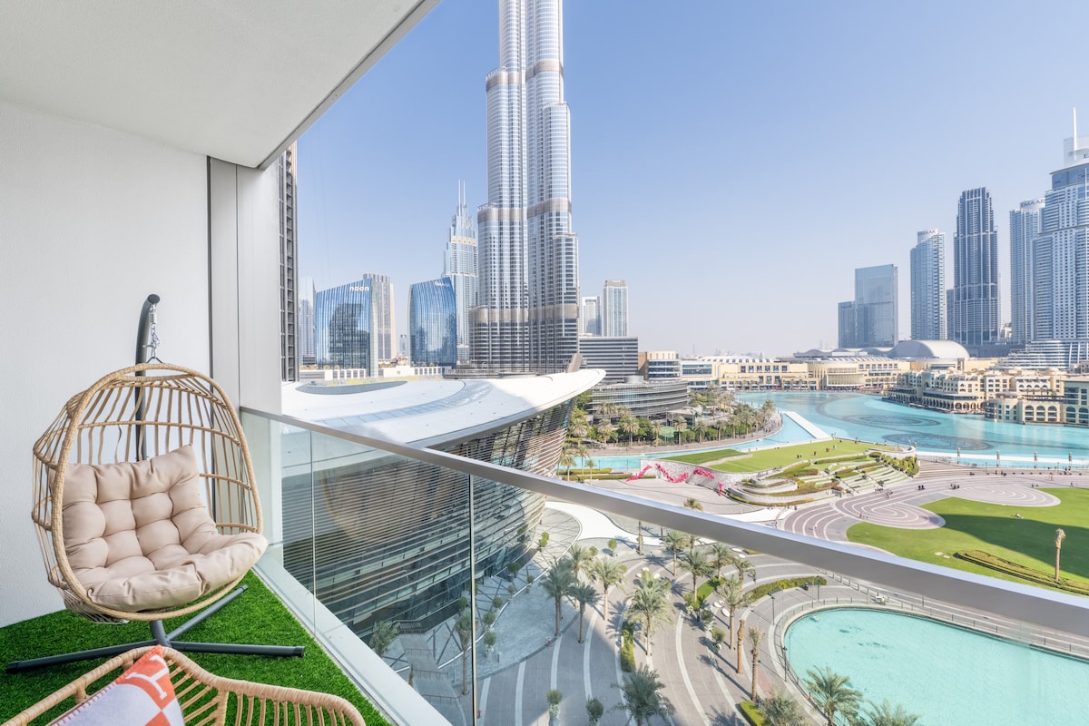 A spacious balcony features a stylish hanging chair with soft cushions, overlooking the vibrant landscape of Downtown Dubai. The view includes the iconic Burj Khalifa and the picturesque waterfront, enhancing the overall appeal of this luxurious setting.