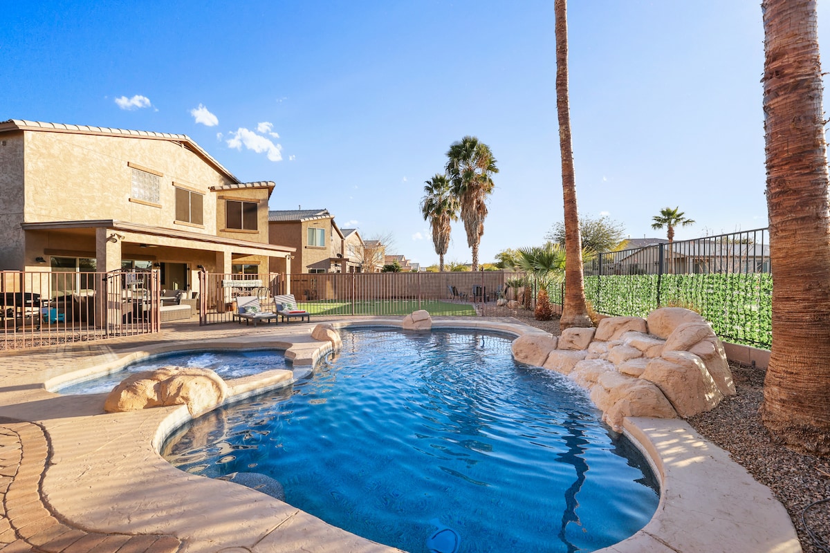 A private heated pool and spa are featured in the backyard, surrounded by a patio area. Palm trees provide shade while a natural stone design enhances the pool's aesthetic. A short fence offers privacy, with a lush green backdrop visible beyond the pool area.