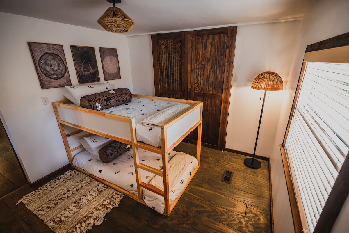 أسرّة بطابقين بحجم مزدوج وخزانة كبيرة وبياضات إضافية وكرسي بين باج وطاولة.